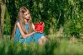 Pensive teen girl sitting on grass at city park and holding red gift box Royalty Free Stock Photo