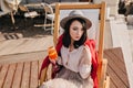 Pensive brunette woman looking away while resting in recliner in sunny day. Outdoor portrait of sad white girl with