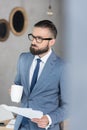 Pensive businessman with coffee cup and papers in hands in office Royalty Free Stock Photo