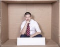 Pensive businessman sitting in a tight box, copy space on white blank board Royalty Free Stock Photo