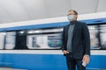 Pensive businessman wears surgical sterile mask to prevent spread of respiratory disease, poses against underground train, travels Royalty Free Stock Photo