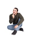 Pensive casual man sitting on the floor smiles looking aside, keeps hand under chin, thoughtful gesture. Lifestyle full length Royalty Free Stock Photo
