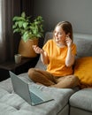 Pensive Caucasian beautiful woman work using laptop headphones remotely from home. Portrait of teenage girl student thinking n