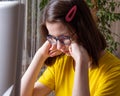 Pensive Caucasian student in a yellow T-shirt thinks, suffers, presses her hands to her face. Distance learning Royalty Free Stock Photo