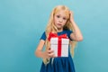 Pensive charming blond girl in a dress with a gift in her hands on a light blue background