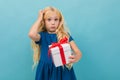 Pensive charming blond young girl in a dress with a gift with a red ribbon in her hands on a light blue background