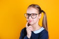 Pensive charming school girl 12 years old in glasses on yellow background