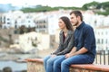 Pensive couple looking away on a ledge on vacation