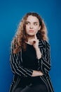 pensive curly girl looks up and thinks about the future on a blue background in a striped jacket