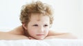 Pensive curly-haired boy lying in bed.