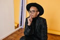 Pensive dark-eyed man looking away and touching his chin. Indoor portrait of carefree african guy in black outfit Royalty Free Stock Photo