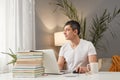 Pensive dreaming Caucasian adult man wearing white T-shirt working at home with laptop freelancer doing his remote work looking Royalty Free Stock Photo