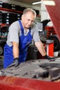 Pensive elderly man mechanic looking at car in auto workshop, determining scope of work