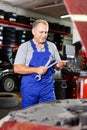Pensive elderly man mechanic looking at car in auto workshop, determining scope of work