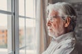 Pensive elderly mature senior man in eyeglasses looking in distance out of window, thinking of personal problems. Lost in thoughts