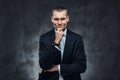 Pensive elegantly dressed handsome man wearing a black classical suit, touching his face and looking at a camera. Royalty Free Stock Photo