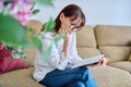 Pensive enthusiastic middle aged woman reading book sitting on sofa Royalty Free Stock Photo