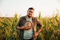 Pensive farmer smiles on face stand in field, took off hat, tired, front view, looking at camera.