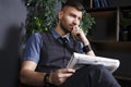 Pensive fashionable confident young handsome man in chair with newspaper in luxurious interior Royalty Free Stock Photo