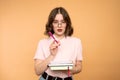 Pensive female writer ponders on new ideas, holds red notebook and pencil near mouth, has thoughtful expression, wears Royalty Free Stock Photo