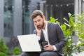 Pensive and focused male businessman working remotely at computer before making a difficult decision sitting near office before