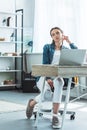 pensive girl in earphones sitting at desk and looking away while using laptop Royalty Free Stock Photo