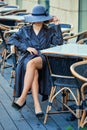 Pensive girl sitting behind a table at cafe terrace in leather coat and felt hat Royalty Free Stock Photo