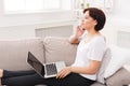 Young thoughtful beautiful woman with phone and laptop on sofa Royalty Free Stock Photo