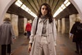 Pensive girl in trench coat with backpack dreamily looking in camera at subway station