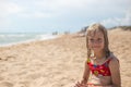 A pensive girl with wet blond hair in a swimsuit sits on the sandy seashore. Summer vacation, travel and tourism Royalty Free Stock Photo
