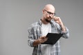 Pensive handsome balded beard with musctache man wearing casual clothes holding clipboard isolated over gray background