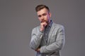 Pensive handsome stylish man in an elegant gray jacket, posing with hand on chin.