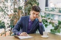 Pensive handsome young man in a business suit works at the table in coffee and holds his head with his hand Royalty Free Stock Photo