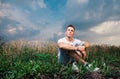 Pensive handsome young man sitting on on the green grass on a ba Royalty Free Stock Photo