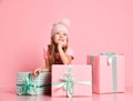 Pensive kid girl is sitting behind gifts boxes presents guessing, dreaming of a present, waiting on pink Royalty Free Stock Photo