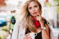 Pensive lady with deep blue eyes posing with cup of tea relaxing after hard week. Outdoor portrait of graceful white