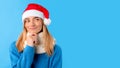 Pensive lady in Santa hat touching chin and looking at copy space, thinking about new year celebration and xmas offer