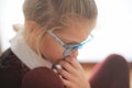 Pensive little beautiful girl in glasses and school uniform thin