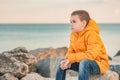 Pensive little boy in an orange jacket by the sea at sunset. Child`s dreams. boy, sea, lifestyle Royalty Free Stock Photo