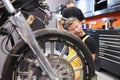 Pensive locksmith holds wrench and looks at motorcycle wheel