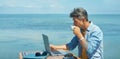 Pensive man freelancer working on laptop computer at beach by blue sea, drinking coffee Royalty Free Stock Photo