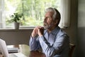 Pensive mature grey haired man sitting at table with laptop