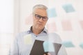 Pensive mature manager looking at sticky notes on glass Royalty Free Stock Photo