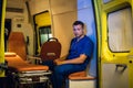 A pensive medical worker in a blue uniform sitting inside the ambulance car and meditating