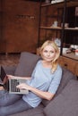 pensive middle aged woman using laptop and looking away while sitting on sofa Royalty Free Stock Photo