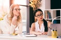 Pensive multiethnic businesswomen in formalwear looking at laptop at office