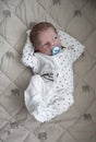 Pensive new born baby boy is laying in white sleepers with blue nipple Royalty Free Stock Photo