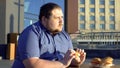 Pensive obese man eating burger, hesitating to start new life, weight loss