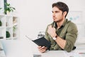 Pensive office manager sitting at desk and holding notebook and pen