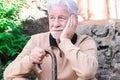 Pensive old senior man in winter sweater outdoors of a rural house leaning on walking stick. Caucasian man with beard and white Royalty Free Stock Photo